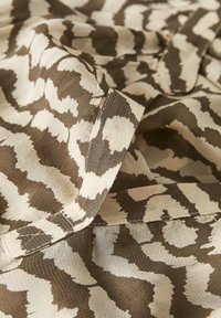 Tissu avec un imprimé animal abstrait marron et crème, présentant une texture douce et des bords cousus, avec des plis créant une apparence en couches.