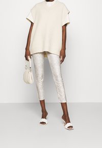 Cream ribbed oversized knit top, silver snake-print cropped pants, white block-heeled sandals, and a small beige shoulder bag.