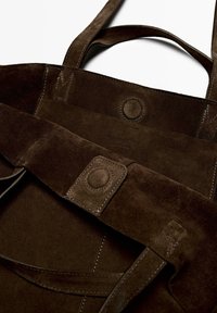 Borsa a spalla in suede marrone con manici doppi, chiusura a pulsante magnetico e dettagli del marchio impresso all'interno. Texture liscia e morbida.
