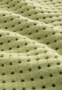 Tessuto a maglia in verde chiaro morbido con una texture a coste e piccoli fori, creando un motivo di aree rialzate e incavate.
