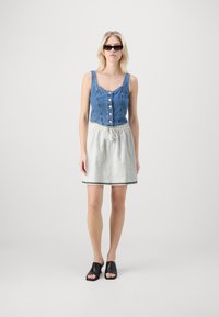 Denim crop felső gombokkal, világosszürke, gumis derekú szoknyával, fekete díszítéssel, és fekete pántos papuccsal párosítva.