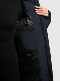 Tengerészkék külső kabát sima, fényes belső béléssel. Cipzáras zseb és patentzárak jellemzik. A texturált anyag látható a széleken.