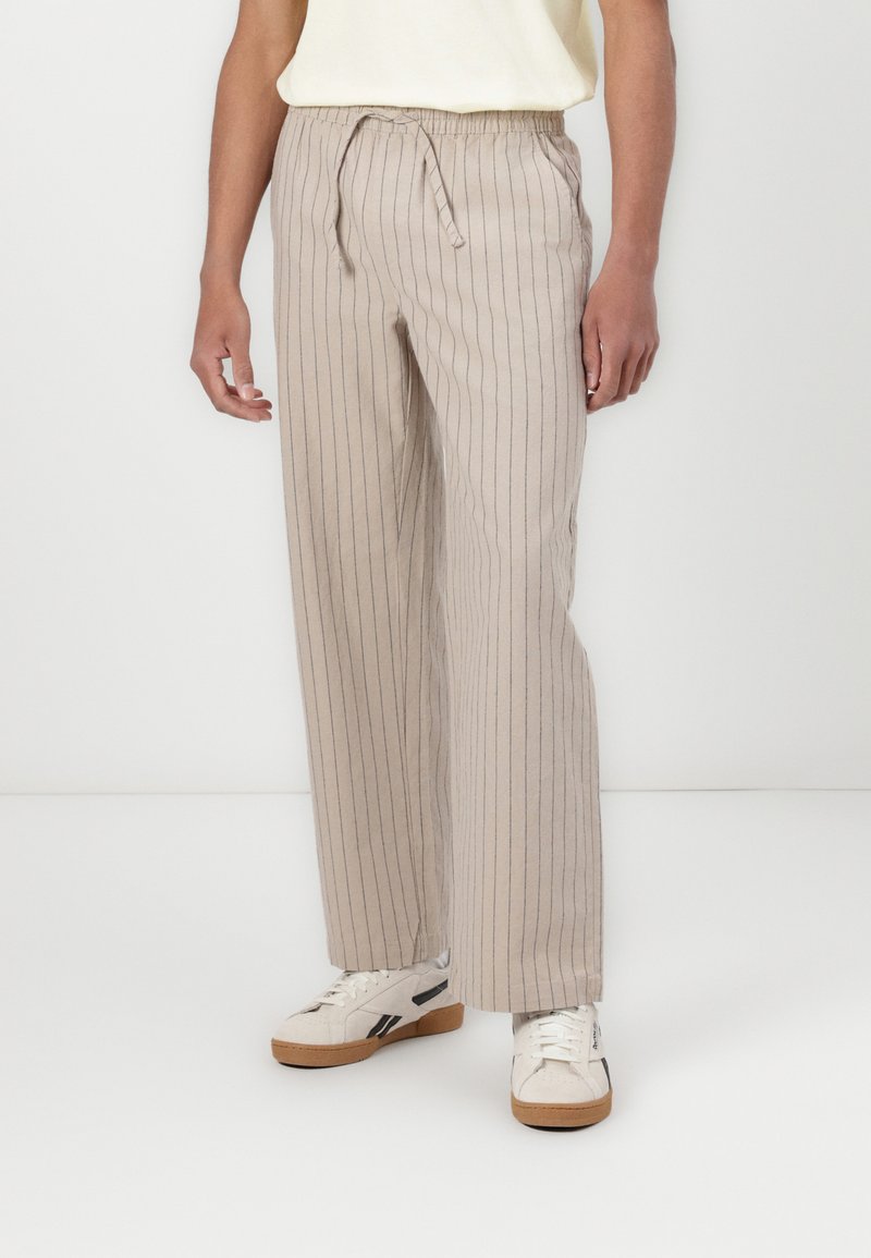Beige gestreifte Leinenmischungshosen mit einem elastischen Bund, Zugband und weitem Bein, kombiniert mit weißen Sneakers.