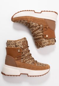 Baskets montantes en suède marron et tissu à motifs avec une semelle intermédiaire blanche et des accents texturés marron. Comprend des lacets et des détails de marque.