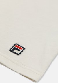 Gros plan sur un tissu blanc montrant un petit logo carré avec un design rouge et bleu marine dans un coin.