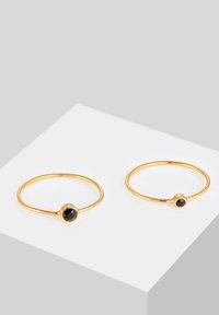 Anelli d'oro con finitura liscia, ciascuno con una pietra nera al centro. Design semplice e minimalista con una banda sottile.