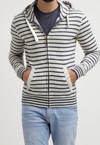 Felpa con zip a righe in grigio chiaro e blu navy, con cappuccio, tasche frontali e lacci. Tessuto morbido con accenti a maglia a contrasto.