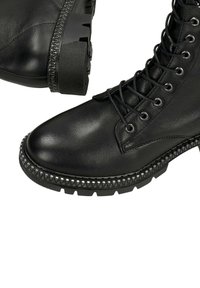 Černé kožené kotníkové boty na šněrování s mohutnými podrážkami a kovovými cvočky podél okrajů podrážek.