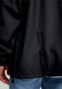 Jachetă neagră impermeabilă, cu un buzunar cu fermoar, șnur ajustabil, textură netedă și un design ajustat pe spate.