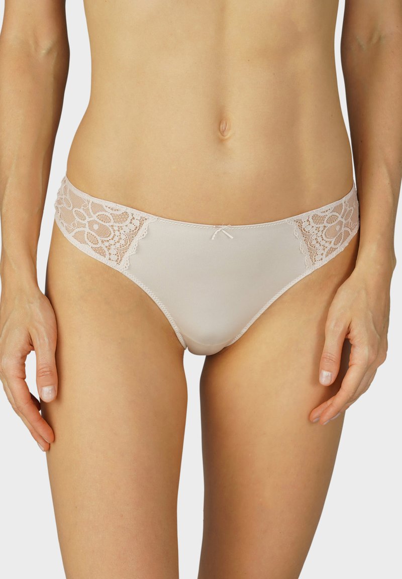 Culotte en dentelle beige avec un motif floral sur les côtés, dotée d'un tissu lisse, d'une coupe taille basse et d'un petit nœud à l'avant.