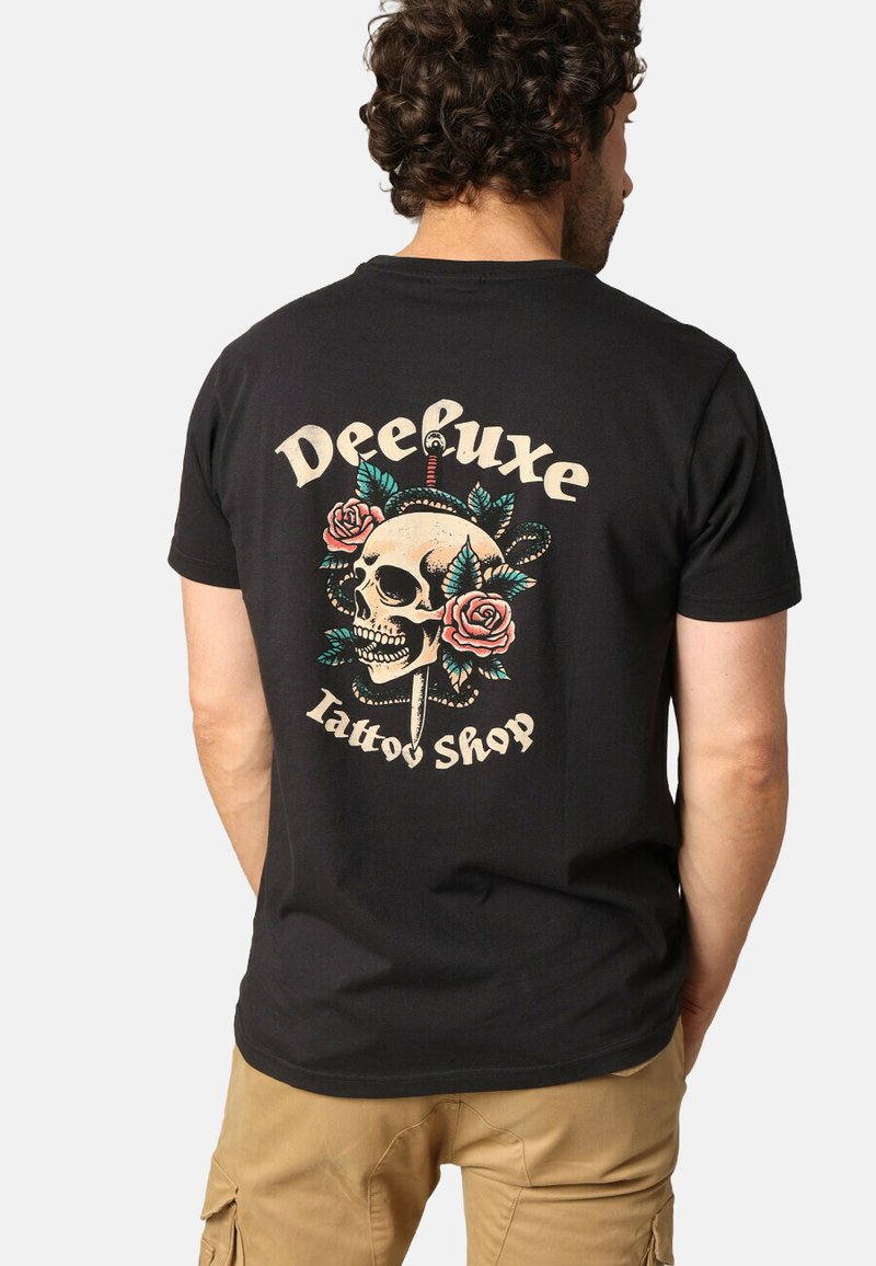 Zwarte katoenen t-shirt met een kleurrijk schedelontwerp met rozen, een slang en de tekst "Deeluxe Tattoo Shop" in een retrolettertype.