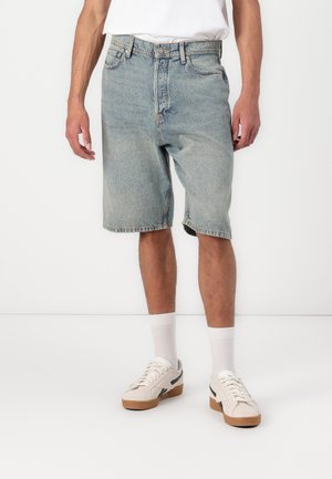 Light blue denim shorts with a relaxed fit, featuring a button and zipper closure, side pockets, and frayed hems. Worn with white socks and sneakers.