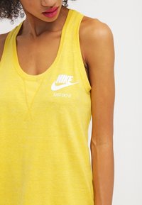 Geel mouwloos tanktop met een gestructureerde afwerking. Voorzien van een witte "Nike"-logo en de tekst "Just Do It" op de voorkant.