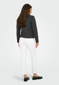 Pull en maille gris foncé ajusté avec des manches longues, associé à un pantalon blanc slim et des mocassins noirs à clous, vu de dos.