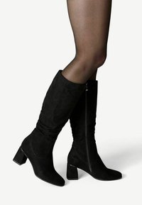 Bottes hautes jusqu'au genou en daim noir avec un talon bloc, une fermeture éclair latérale et une texture froncée sur la partie supérieure. Conception à bout lisse et plat.
