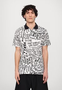Camisa polo de manga curta com um padrão de texto em preto e branco, gola de malha preta e ajuste relaxado. Feita de tecido leve.
