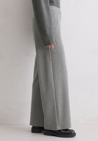 Pantalon large gris à côtes avec une texture douce, doté d'une taille haute, associé à des chaussures noires épaisses. Vue de côté.