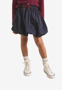 Marineblauwe rok met elastische tailleband, gatherende stof en een trekkoord, gecombineerd met witte hoge sneakers en crew-sokken.