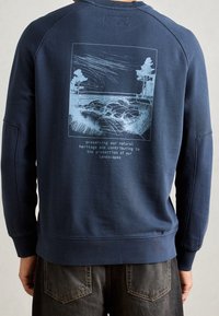 Felpa blu navy con maniche a raglan, caratterizzata da un'illustrazione paesaggistica stampata in azzurro e testo sul retro. Tessuto morbido in misto cotone.