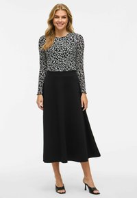 Longue jupe noire associée à un haut ajusté avec un motif de points noir et blanc, à manches longues et en tissu lisse.