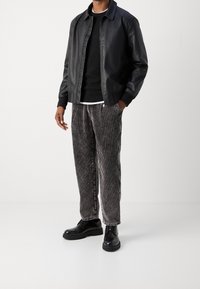 Zwarte leren jas over een zwarte trui en een wit T-shirt, gecombineerd met grijs gestreepte corduroy broek en zwarte veterschoenen.