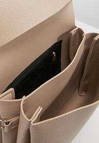 Borsa a tracolla in pelle beige con una tasca interna con zip nera. Design aperto che mette in mostra un ampio interno e doppie sezioni.
