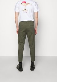 Olivgrön tapered byxor med en slät textur, med bakfickor. Bärs med en vit t-shirt med grafik och svarta ankelstövlar.