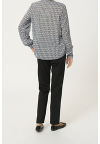 Svart och vit långärmad skjorta med geometriskt mönster, kombinerad med svarta byxor och blanka svarta platta skor. Bakvy, ljus bakgrund.