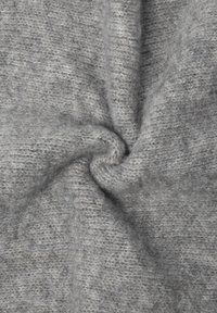 Tissu en laine tricotée doux et gris, torsadé au centre, montrant la texture et la douceur du matériau.