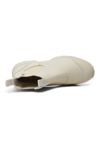 Zapato slip-on de color beige claro hecho de cuero suave, con inserciones elásticas en los laterales y una suela de goma texturizada. Punta redondeada y lengüeta en el talón.