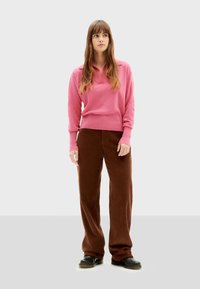 Roze gebreide trui met een kraag, gecombineerd met bruin hoge taille wijde broek. De outfit heeft een zachte textuur en een relaxte pasvorm.