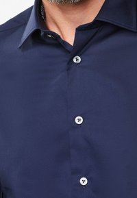 Navy blue dress shirt featuring a classic collar, smooth texture, and four button closures with contrasting stitching details.