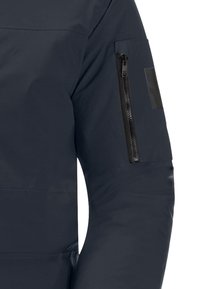Giacca navy realizzata in un tessuto liscio e opaco. Include una tasca con zip sul braccio superiore, con finiture nere e una discreta applicazione del logo.