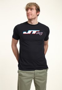 Svart kortärmad t-shirt i slät tyg med en kontrasterande "JT Racing"-logotyp i rött och blått över bröstet.