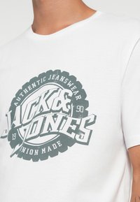 Hvit bomulls t-skjorte med et stort grønt grafisk trykk, sirkulært design med teksten "JACK & JONES" og slitt tekstur.