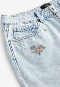 Jean en denim bleu clair avec une petite broderie florale rose et verte près de la poche avant et un rivet métallique visible ainsi qu'une boucle de ceinture.