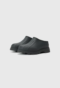 Black rubber clogs with a rounded toe, textured upper, and chunky sole featuring a deep tread for grip. Lightweight and slip-on design.
