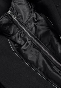 Gros plan sur une veste noire montrant une fermeture éclair argentée partiellement ouverte avec une doublure en tissu lisse et brillant à l'intérieur.