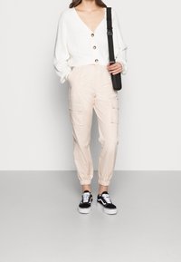 Vit ribbad cardigan med träknappar, i kombination med ljusbeige cargobyxor med fickor och elastiska muddar. Svart och vita sneakers.