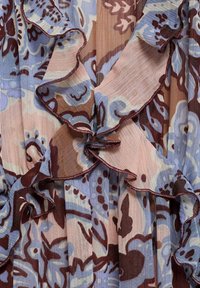 Zavazovací top z plisované tkaniny s volánkovými okraji, který má květinový vzor v jemné modré, hnědé a růžové barvě. Lehké a strukturované.