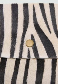 Borsa a pochette in stampa zebra con una morbida texture in pelliccia sintetica; presenta audaci strisce nere su uno sfondo crema e una chiusura tonda dorata a scatto.