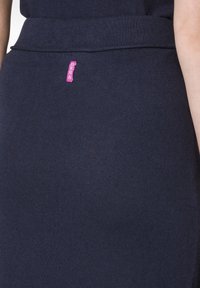 Fustă bleumarin dintr-un material moale, cu o textură netedă. Prezintă un brâu orizontal și un eticheta roz a brandului cusută pe lateral.