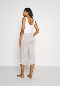White tank top paired with light striped cropped pants, featuring an elastic waistband and a loose fit. Model stands barefoot with hair down.