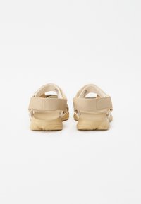 Light beige sandals with adjustable straps, cushioned soles, and a textured, durable outer material. Features a simplistic, modern design.