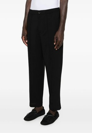 Uomo con pantaloni neri su misura e scarpe nere stile mocassino su sfondo bianco.