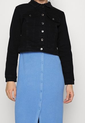 Chaqueta corta de mezclilla negra con botones plateados sobre un vestido abotonado de canalé azul claro.