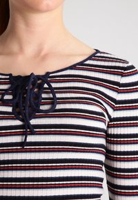 Randig topp med rund halsringning, i marinblått, rött och vitt horisontellt mönster. Ribbad textur och snörningsdetalj framtill.