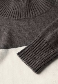 Grauer und cremefarbener gestrickter Pullover mit einem gerippten Kragen und Bündchen sowie einem Farbblockdesign. Weicher Stoff und mittelschwere Ware.