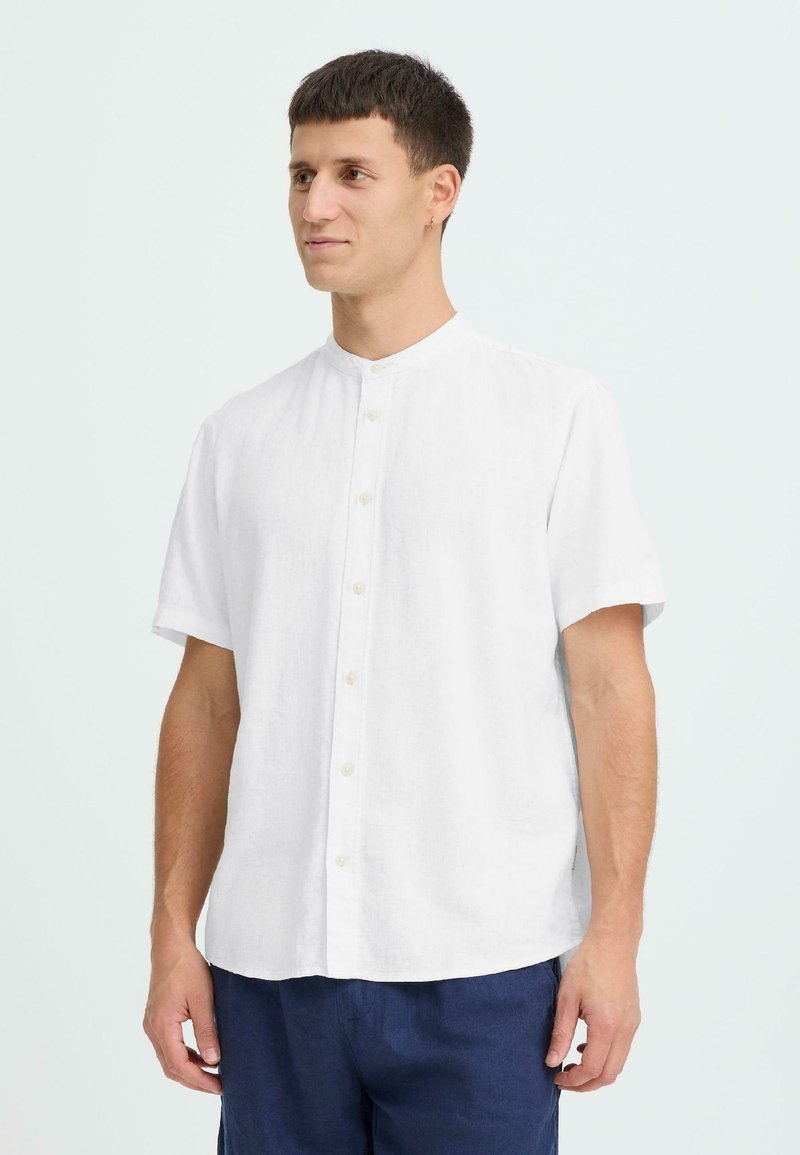 Chemise blanche en lin à manches courtes avec un col mandarin, dotée d'une fermeture boutonnée à l'avant et d'une coupe décontractée. Texture lisse, design simple.
