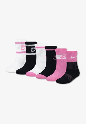 Six paires de chaussettes montantes Nike en blanc, noir et rose, avec des logos contrastants et des accents au talon et aux orteils, disposées en rangée sur un fond blanc.